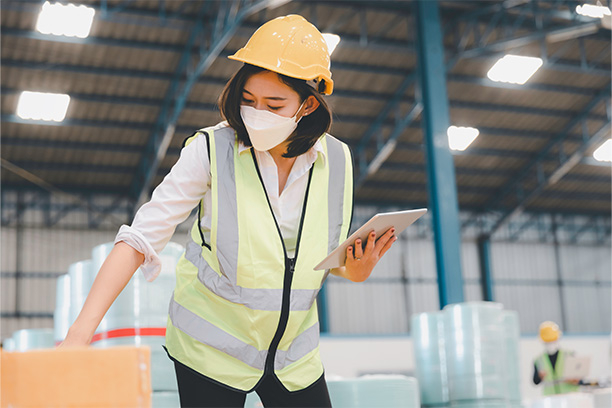 Woman at a warehouse looking at packages and comparing it to her tablet