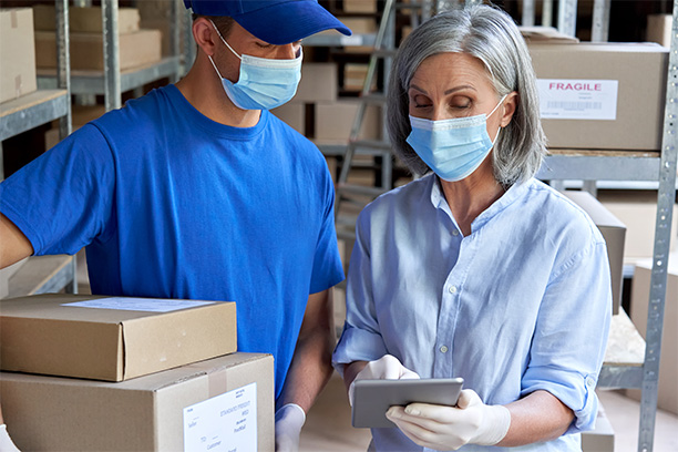 Two employees at a medical warehouse moving boxes and dealing with logistics on a tablet